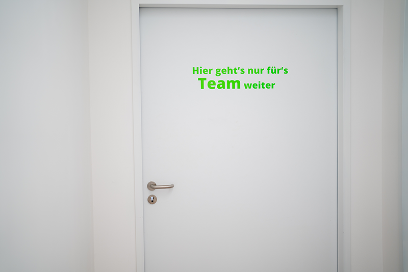 Weiße Tür mit grünem Schriftzug „Hier geht’s nur fürs Team weiter“.